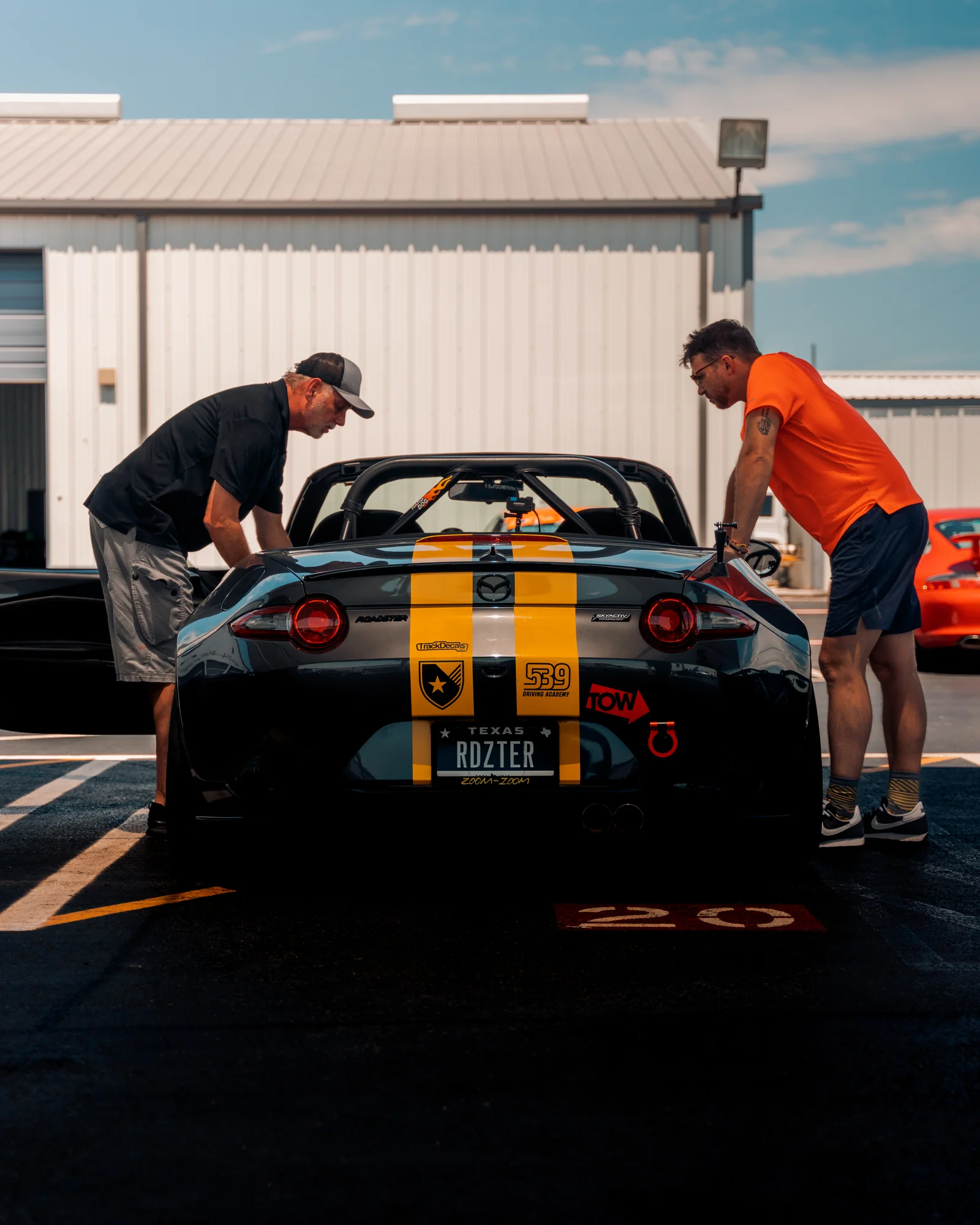 Two people beside a black sports car with yellow stripes in the paddock